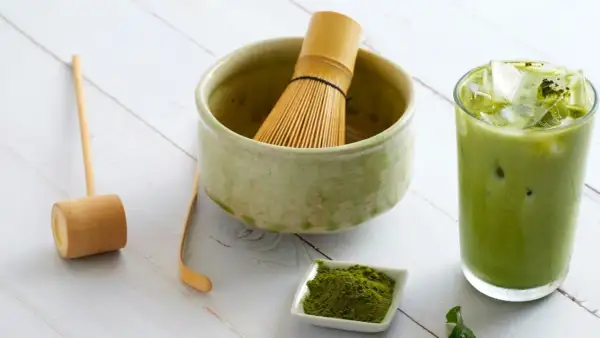 Akcesoria do przygotowania matcha: bambusowa miotełka, miarka, miseczka z proszkiem i szklanka z zielonym napojem. Idealny przepis na matche.